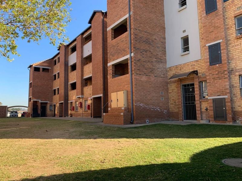 Exterior view of a multi-story apartment building featuring face brick construction, security gates, and communal lawn area.