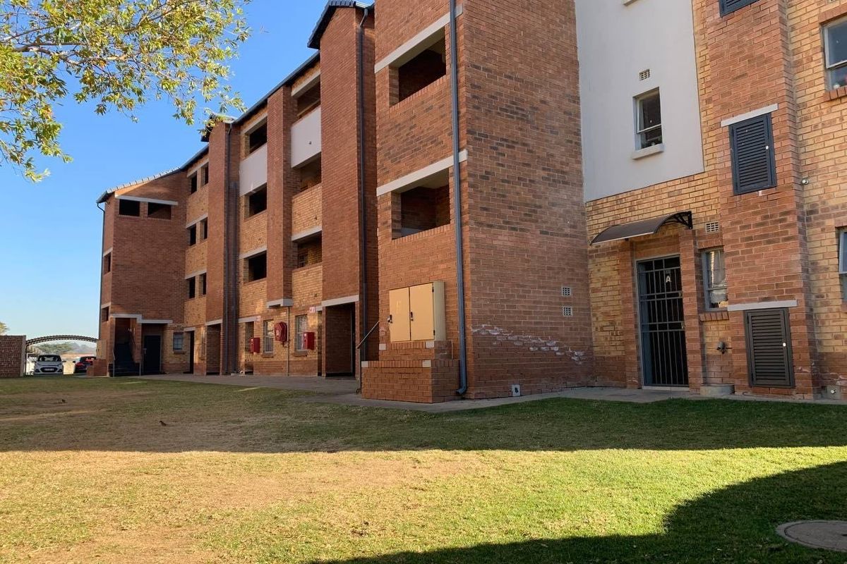 Exterior view of a multi-story apartment building featuring face brick construction, security gates, and communal lawn area.