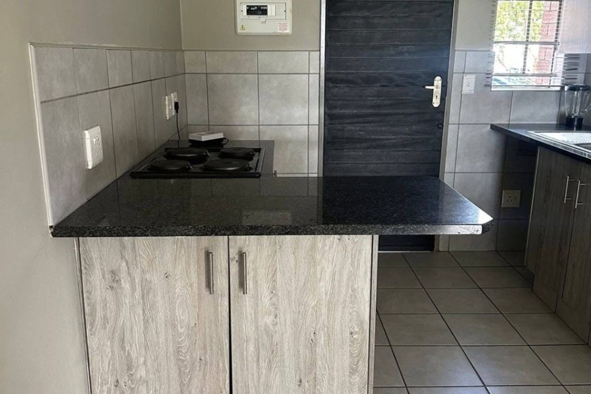 A functional kitchen featuring wood-look cabinetry, granite countertops, an integrated electric hob, and neutral tiled flooring with a clean, modern aesthetic.