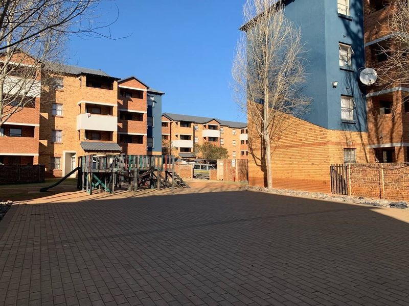 A view of the apartment complex courtyard featuring paved ground, brick building facades, and a communal playground area.