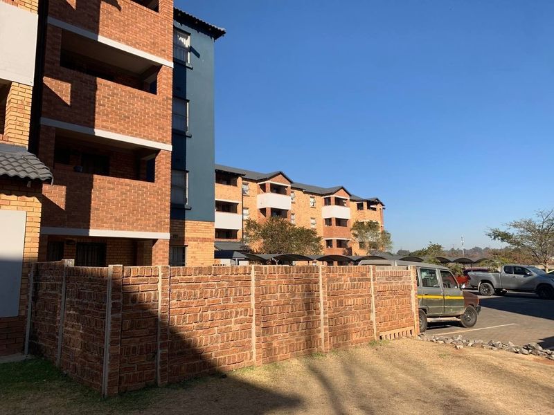 Exterior view of a multi-story apartment complex featuring face brick construction, tiled roofing, and an adjacent paved parking area.