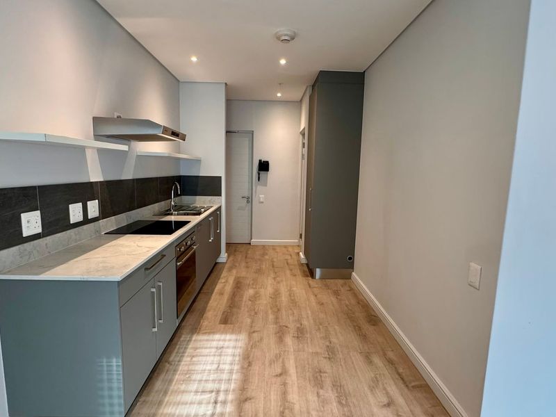 Modern galley-style kitchen featuring sleek grey cabinetry, stone countertops, integrated appliances, and light wood-look laminate flooring in a clean, minimalist space.