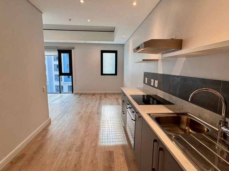 Modern open-plan kitchen and living area featuring sleek cabinetry, integrated appliances, laminate flooring, and recessed lighting in a bright, contemporary apartment setting.