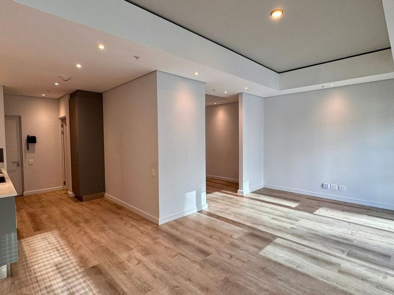 A bright, modern open-plan living and kitchen area featuring recessed ceiling details, contemporary cabinetry, and high-quality laminate flooring throughout.