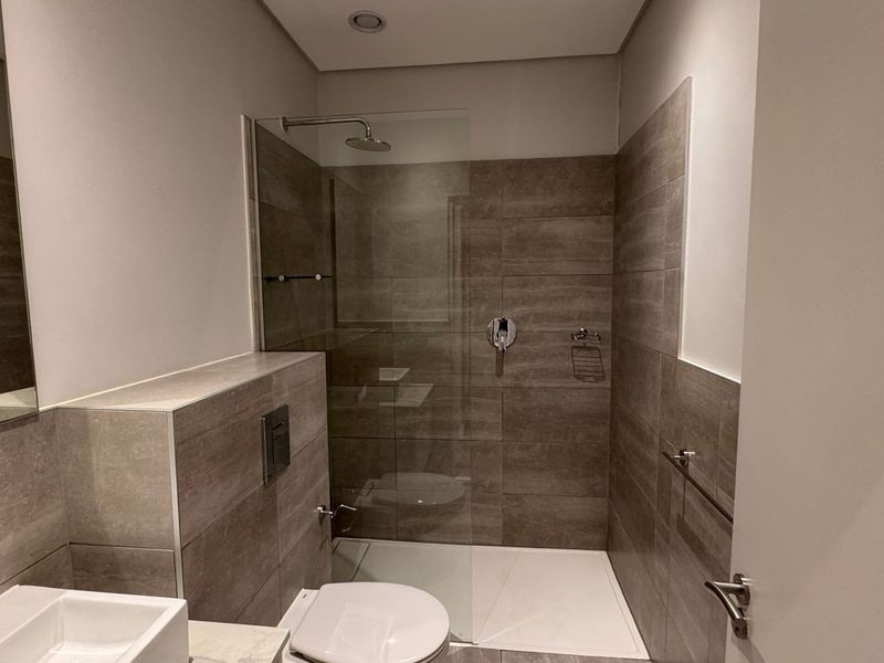 Modern bathroom featuring a walk-in shower with glass screen, wall-mounted toilet, and contemporary vanity basin with neutral tiled finishes.