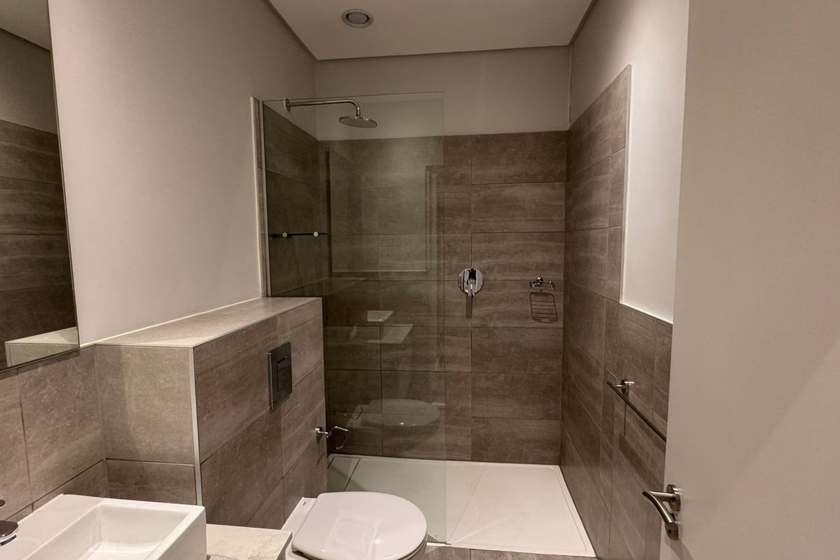 Modern bathroom featuring a walk-in shower with glass screen, wall-mounted toilet, and contemporary vanity basin with neutral tiled finishes.