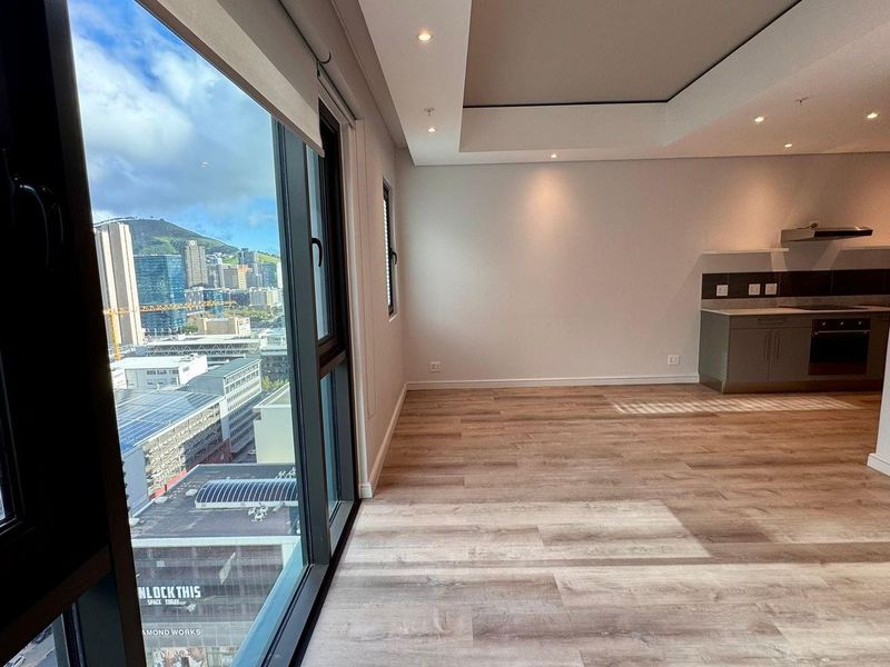 Modern open-plan living area featuring laminate flooring, recessed lighting, and a compact kitchen with built-in appliances, complemented by expansive city views.
