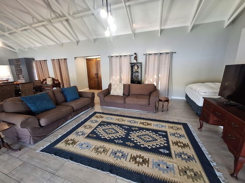 Spacious open-plan living area featuring high vaulted ceilings with exposed rafters, tiled flooring, and double wooden doors leading to adjacent spaces.
