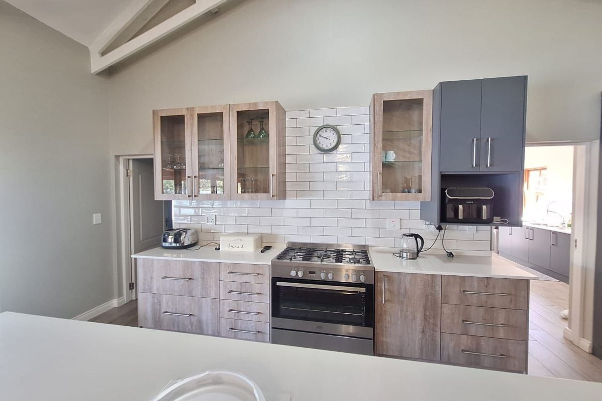 Modern kitchen featuring light wood-tone cabinetry, contrasting grey upper cabinets, white quartz countertops, subway tile backsplash, and a gas range with vaulted ceilings.