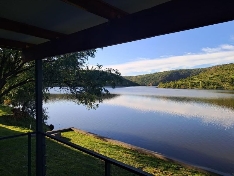A scenic view of a tranquil lake and surrounding hills, captured from a covered patio area with a metal railing.