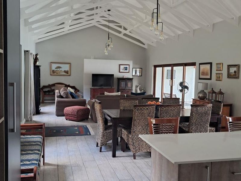 Spacious open-plan living and dining area featuring high vaulted ceilings with exposed white trusses, modern tiled flooring, and seamless access to the outdoor patio.