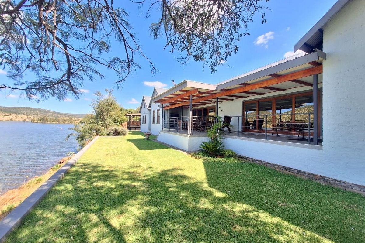 Spacious rear exterior featuring a covered patio with timber pergola, overlooking a well-maintained lawn and waterfront views.