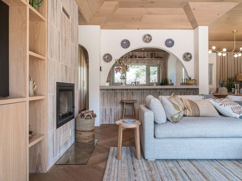 A beautifully designed open-plan living area featuring a modern fireplace, timber ceiling, herringbone flooring, and an arched pass-through to the kitchen area.