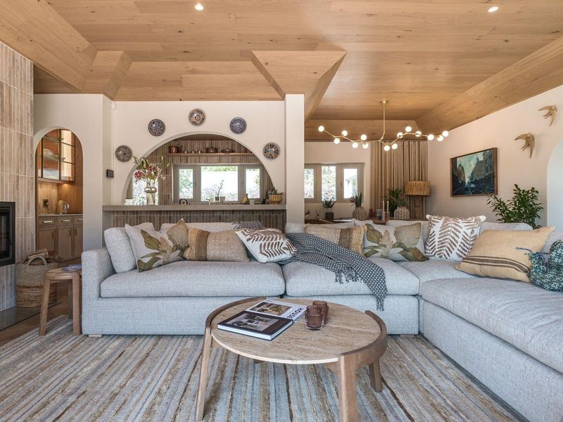 Spacious open-plan living area featuring a warm timber ceiling, built-in fireplace with tiled surround, and elegant arched architectural details.