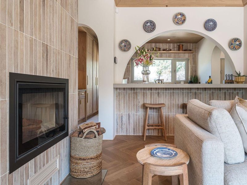 A beautifully designed open-plan living area featuring a modern built-in fireplace, herringbone timber flooring, and a stylish arched breakfast bar with tiled finishes.