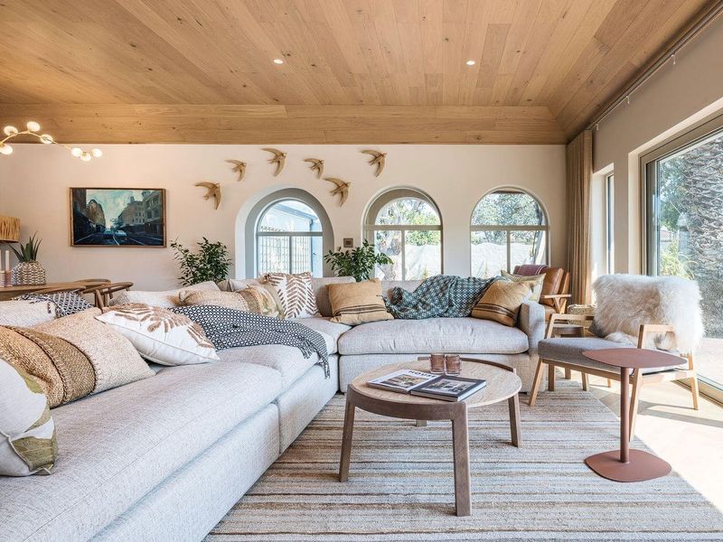 Spacious living room featuring a warm timber-clad vaulted ceiling, arched windows, and large sliding glass doors that provide abundant natural light.