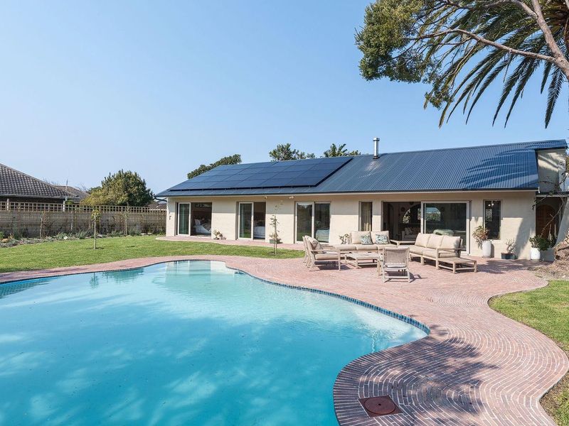 Spacious rear garden featuring a swimming pool, brick paved patio area, and a house exterior equipped with roof-mounted solar panels.