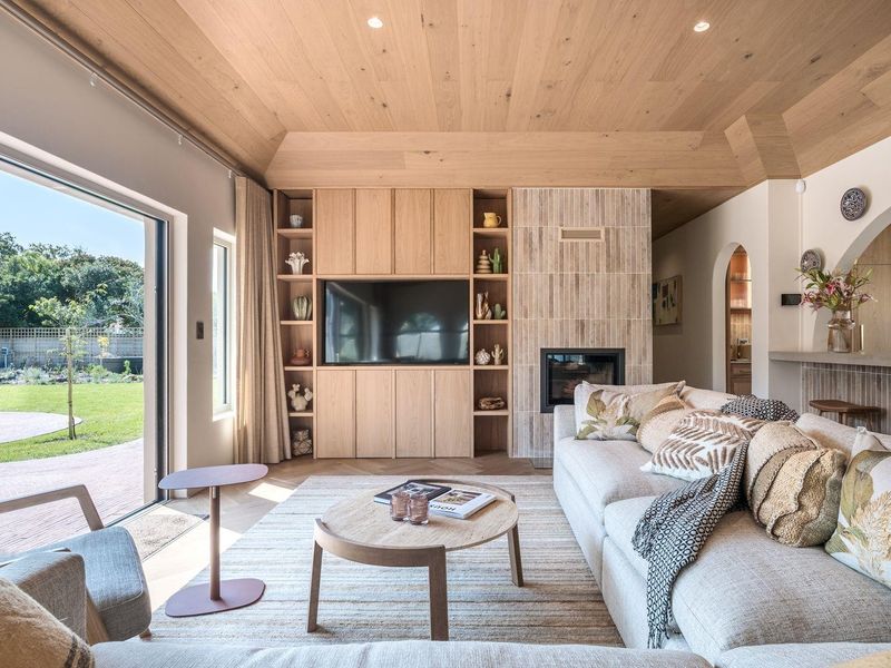 A bright, modern living room featuring custom built-in cabinetry, a tiled fireplace, and a timber-clad ceiling with direct access to the garden.