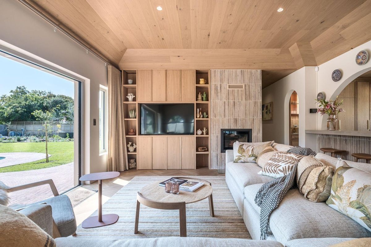 A bright, modern living room featuring custom built-in cabinetry, a tiled fireplace, and a timber-clad ceiling with direct access to the garden.