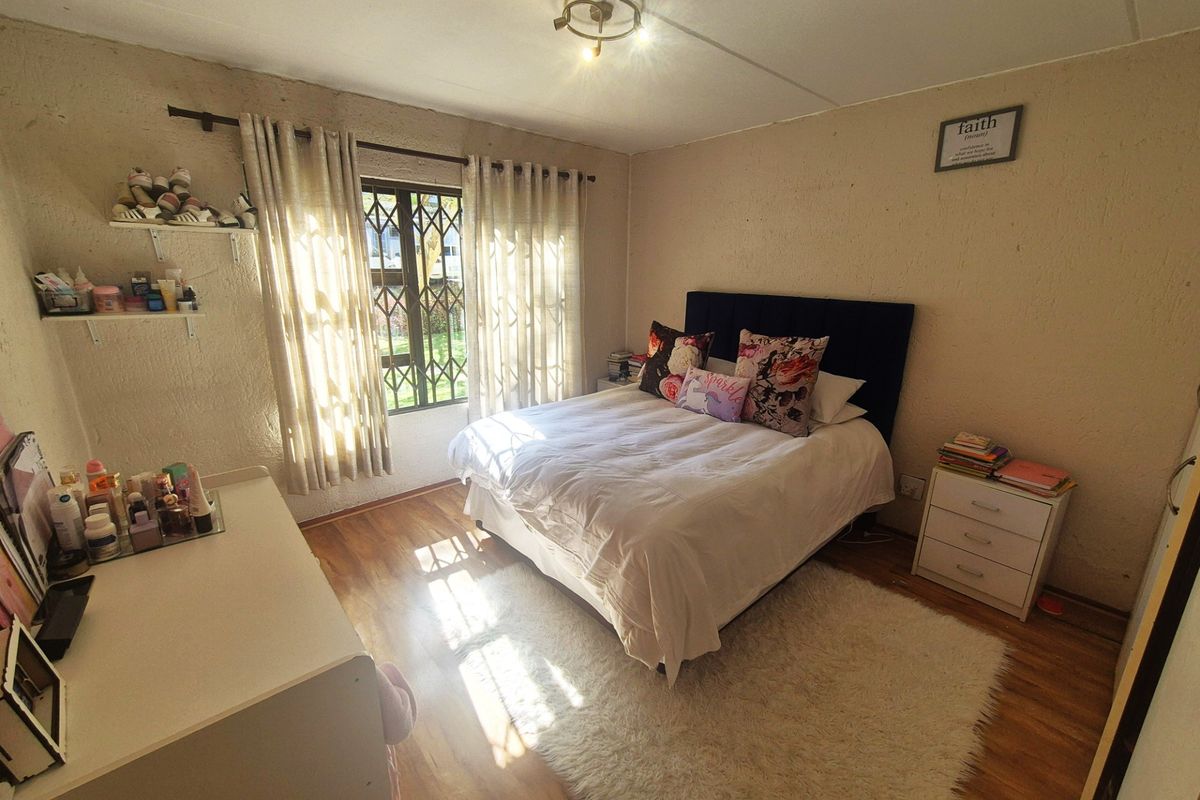 A bedroom featuring laminate flooring, textured walls, and security burglar bars on the window, providing a functional living space.