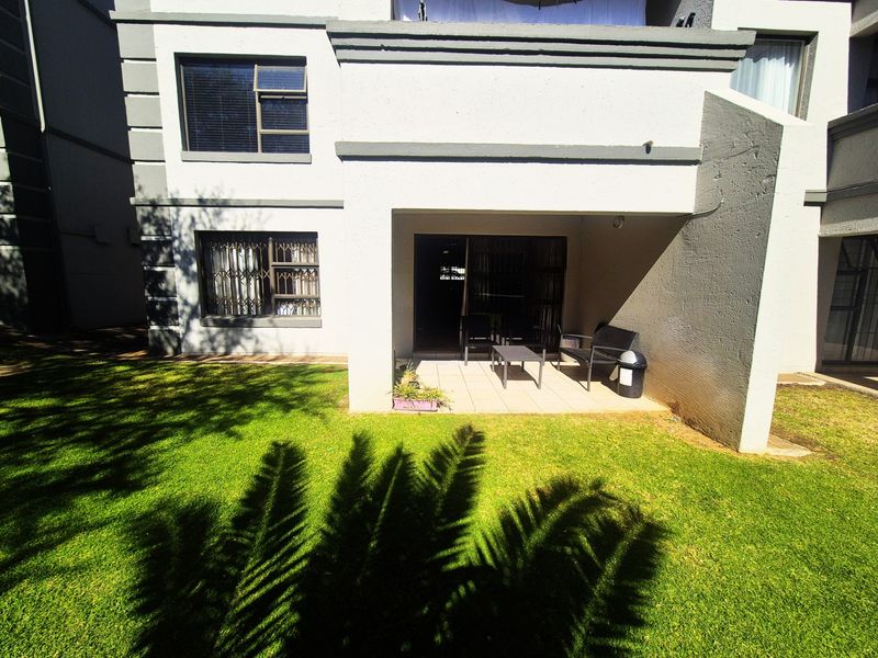 Rear view of the apartment featuring a covered tiled patio area leading onto a private lawn with security gates and sliding door access.