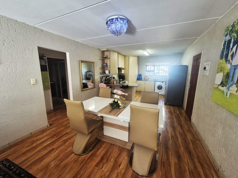 Open-plan living and dining area featuring laminate flooring, textured walls, and a functional kitchen with built-in cabinetry and a breakfast counter.