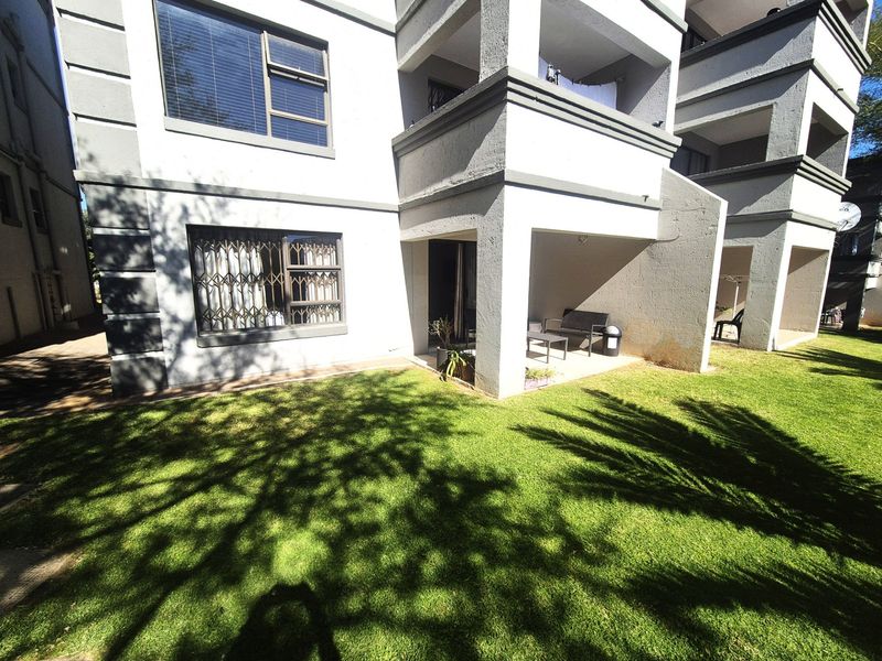 Rear view of the apartment building featuring a covered patio area, security bars on windows, and a well-maintained communal lawn.