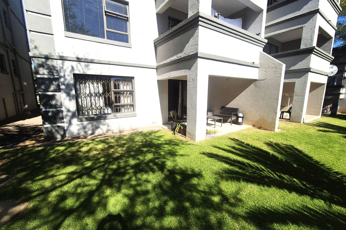 Rear view of the apartment building featuring a covered patio area, security bars on windows, and a well-maintained communal lawn.