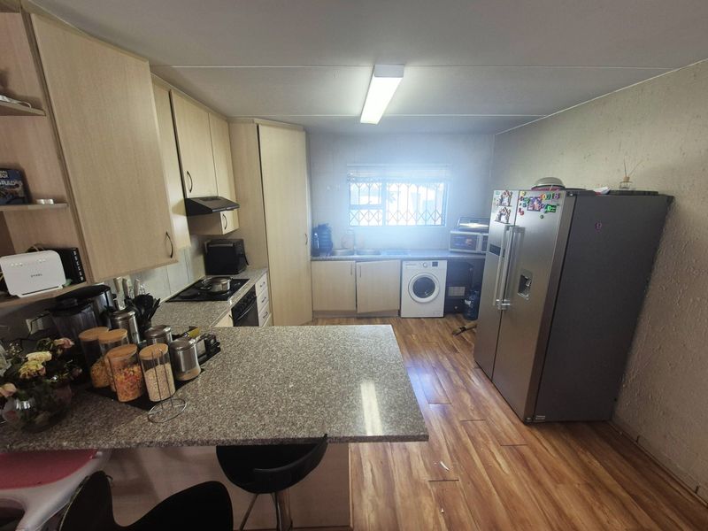 Functional kitchen featuring laminate cabinetry, granite countertops, a breakfast bar, and integrated appliances, with a window providing natural light and security bars.