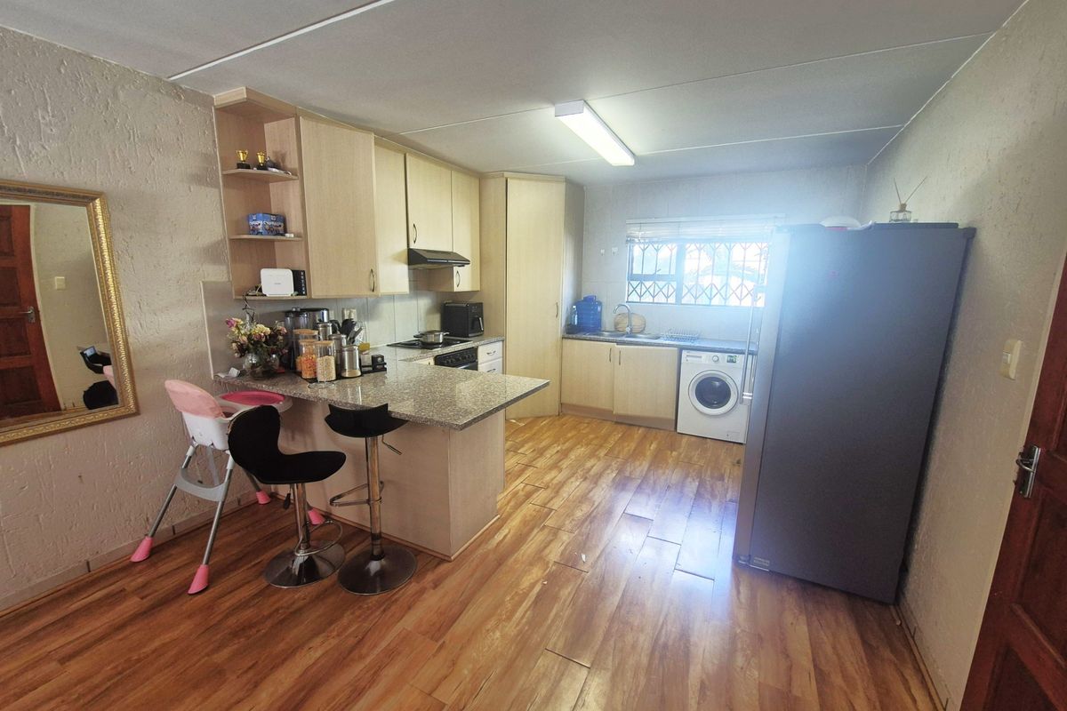 Functional kitchen featuring laminate flooring, granite countertops, built-in cabinetry, a breakfast bar, and integrated appliances including a hob and extractor fan.