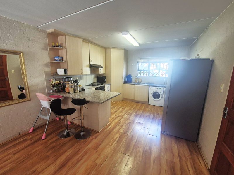 Functional kitchen featuring laminate flooring, granite countertops, built-in cabinetry, a breakfast bar, and integrated appliances including a hob and extractor fan.