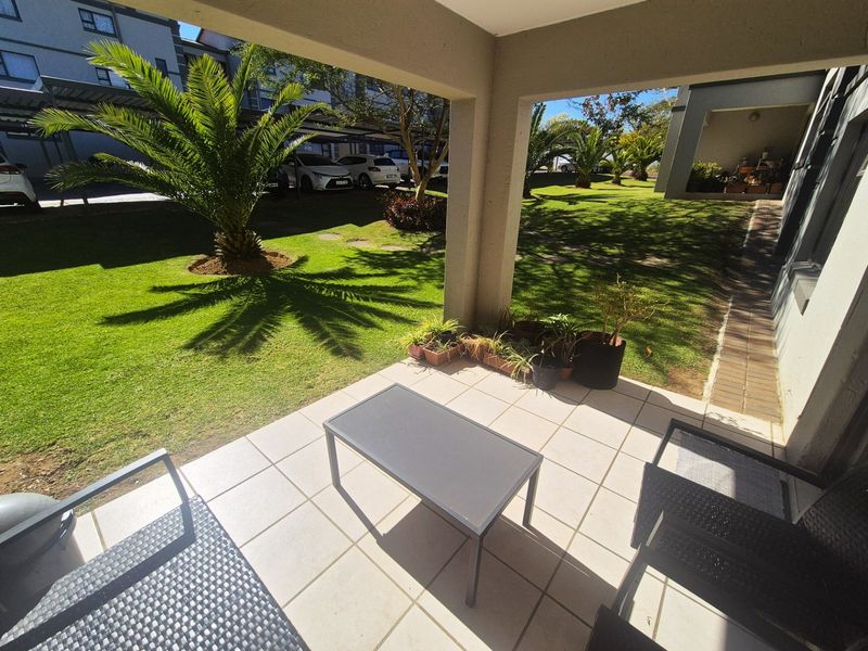 A covered patio area with tiled flooring, overlooking a well-maintained communal garden and parking area.