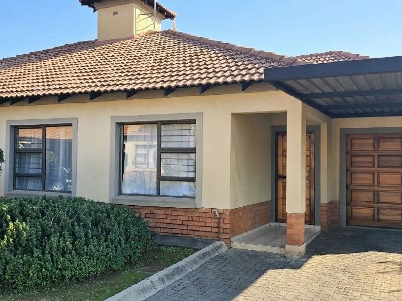 Front elevation of a townhouse featuring a tiled roof, brick accents, a paved driveway, and an integrated carport with a wooden garage door.