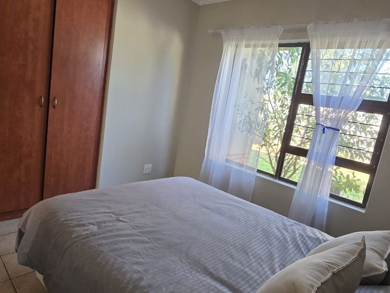 A functional bedroom featuring built-in wooden cupboards, tiled flooring, and a window fitted with security bars for added safety.