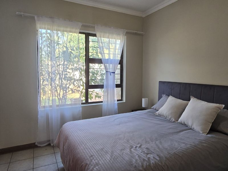 A functional bedroom featuring tiled flooring, a window with security bars, and a built-in cupboard, offering a neutral and practical living space.