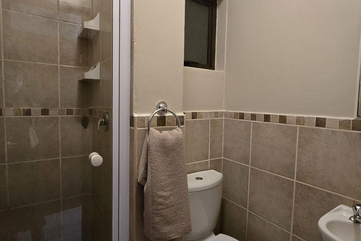 A functional bathroom featuring a shower enclosure, wall-mounted basin, and neutral tiled walls with a decorative border.
