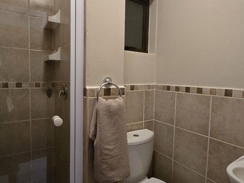 A functional bathroom featuring a shower enclosure, wall-mounted basin, and neutral tiled walls with a decorative border.