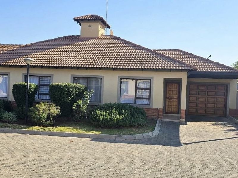 Front elevation of a townhouse featuring a tiled roof, brick driveway, integrated garage, and established garden landscaping.