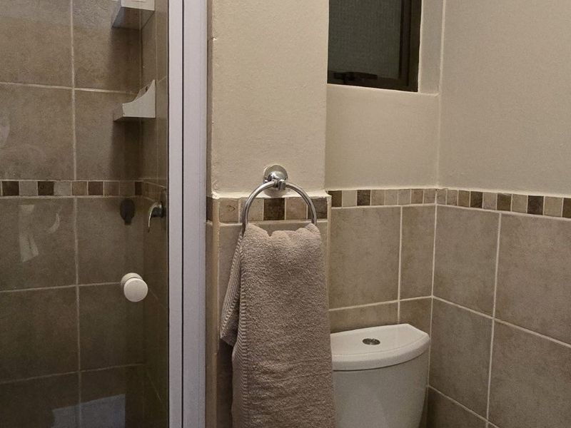 A functional bathroom featuring a shower enclosure, toilet, and neutral tiled finishes with decorative border accents.