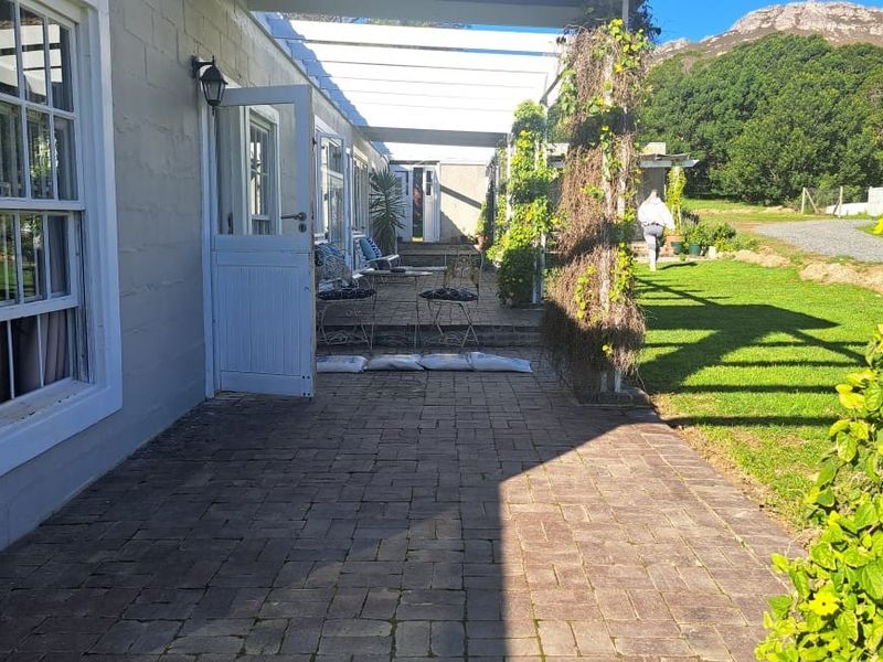 A paved outdoor patio area featuring a pergola structure, sash windows, and direct access to the garden through a stable door.