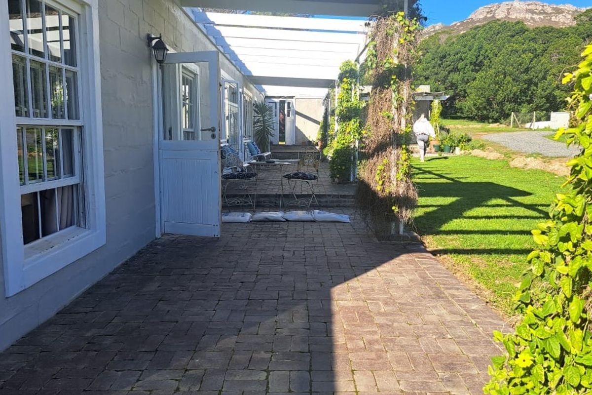 A paved outdoor patio area featuring a pergola structure, sash windows, and direct access to the garden through a stable door.