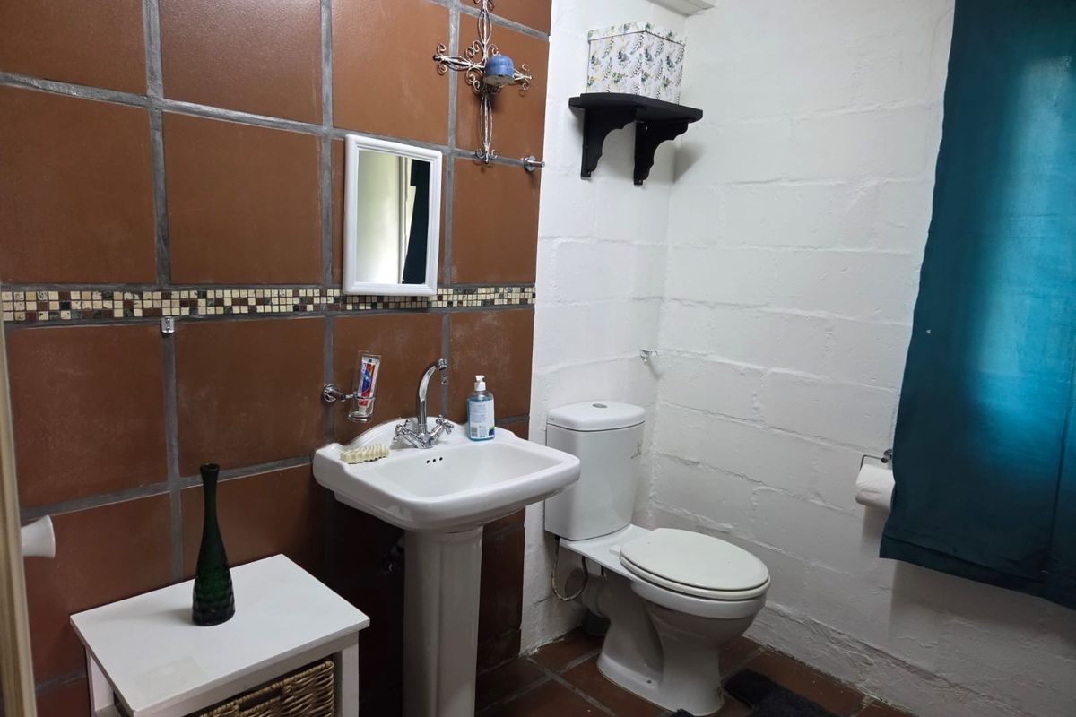 A functional bathroom featuring a pedestal sink, toilet, and a combination of brown tiled and painted block walls.