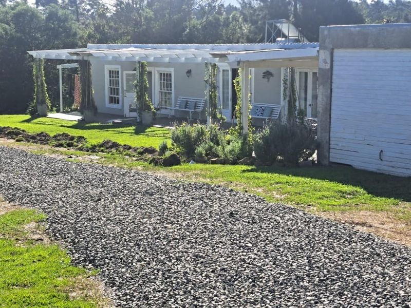 Front view of the property featuring a gravel driveway, attached garage, and a covered pergola area with access through french doors.
