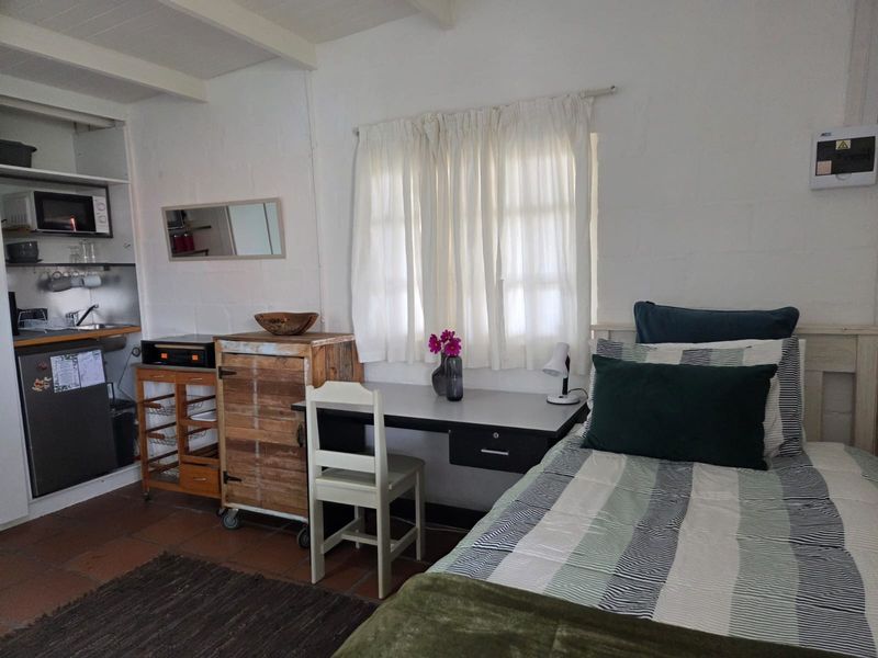 A compact open-plan studio space featuring a small kitchenette with sink, exposed ceiling beams, and tiled flooring, suitable for efficient living.