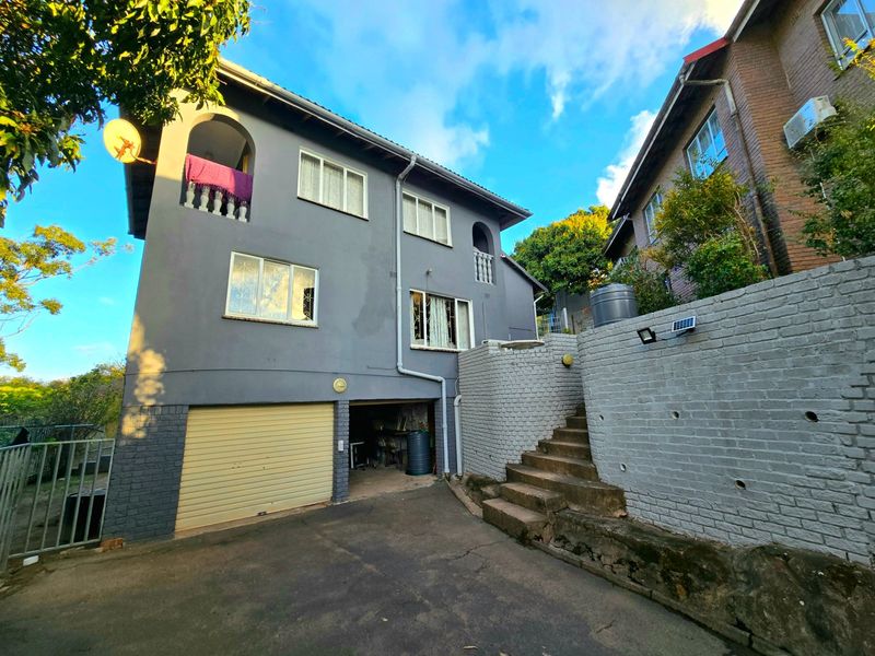 Rear view of a multi-story house featuring a garage, external staircase, and balcony with security bars on windows.