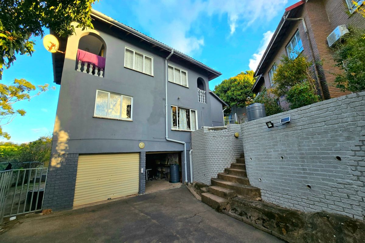 Rear view of a multi-story house featuring a garage, external staircase, and balcony with security bars on windows.
