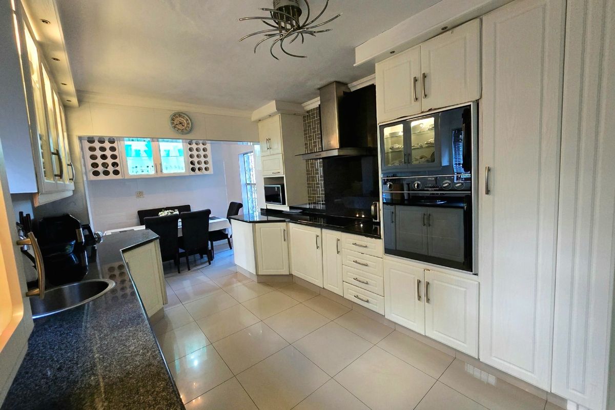 A well-maintained kitchen featuring granite countertops, built-in cabinetry, integrated oven, and modern tiled flooring, with an adjacent dining area.