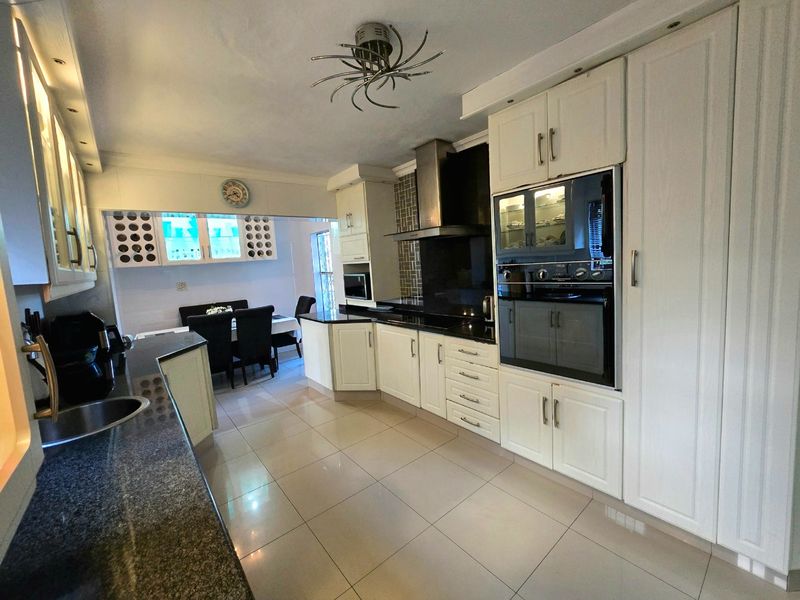 A well-maintained kitchen featuring granite countertops, built-in cabinetry, integrated oven, and modern tiled flooring, with an adjacent dining area.