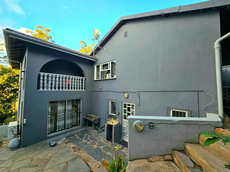 Rear exterior view of the house featuring a stone-paved patio, a balcony with a balustrade, and external utility areas.