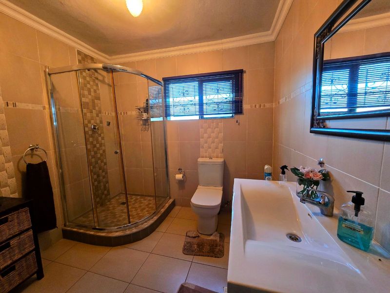 A well-maintained bathroom featuring a curved glass shower enclosure, tiled walls and flooring, a modern washbasin, and a wall-mounted toilet.